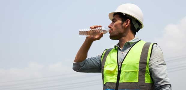 man in yellow vet and white hard hat drinking a bottle of water against a blue sky